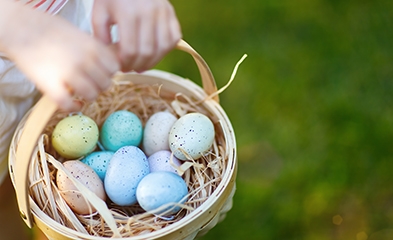 Child holding wicker basket filled with colorful dyed eggs