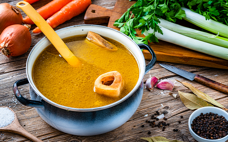 Bowl of soup on table surrounded by vegetables