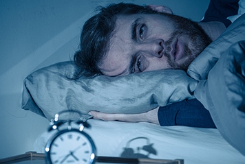 Man awake in bed, alarm clock in foreground