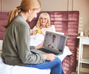 Older woman in bed resting, younger woman on video call with healthcare provider