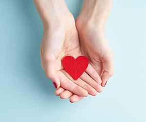 Cupped hands holding a red paper heart