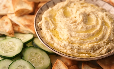 Bowl of hummus surrounded by vegetables and pita