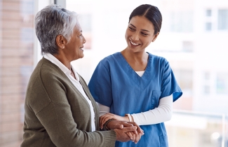 Healthcare working in scrubs walking with older woman