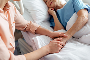 Visitor holding hand of patient in hospital bed