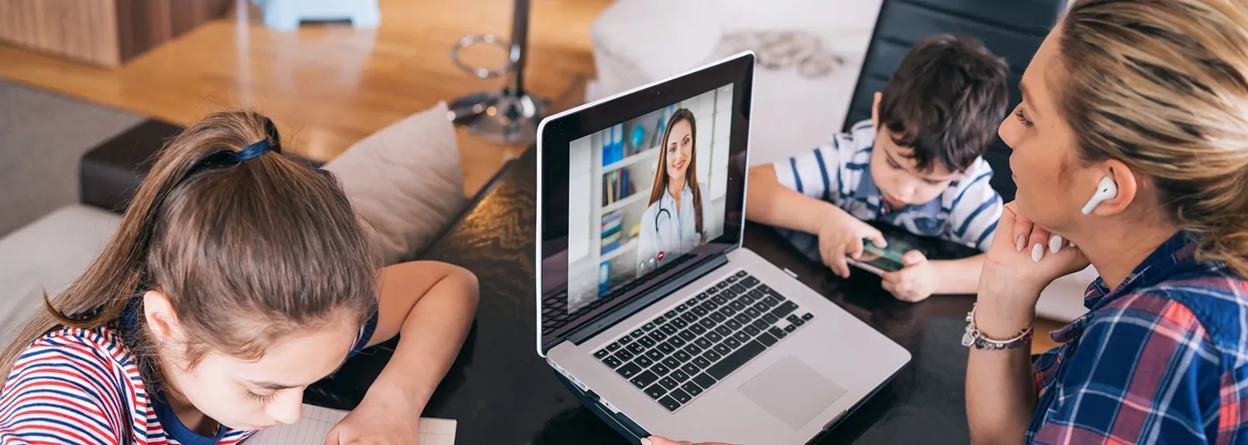 Family around table, woman on laptop on video chat with healthcare provider